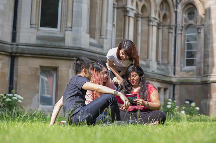 Students reading a brochure sat on grass
