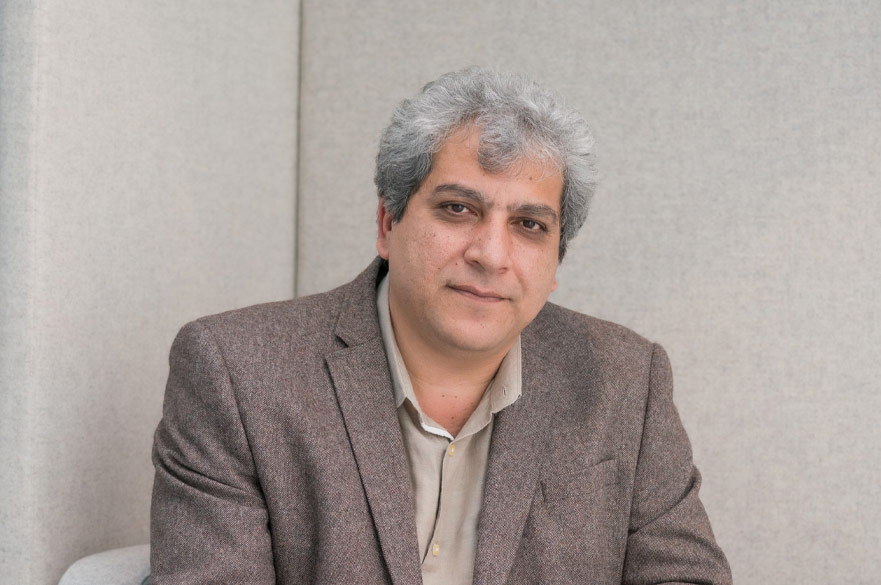 A grey-haired man in a grey jacket and khaki shirt looking into the camera.
