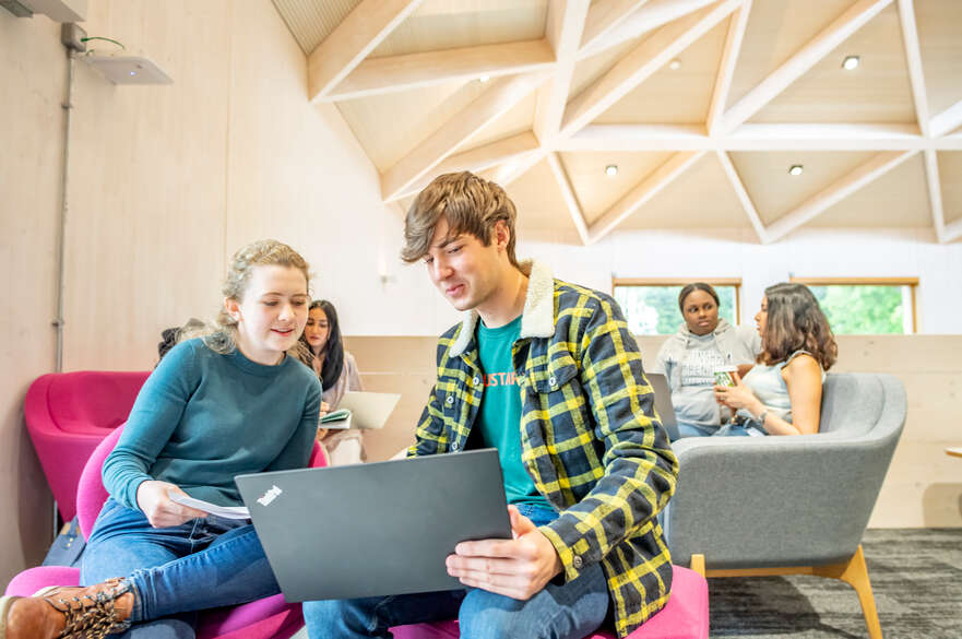 Three pairs of students confer over laptops in a lounge area.