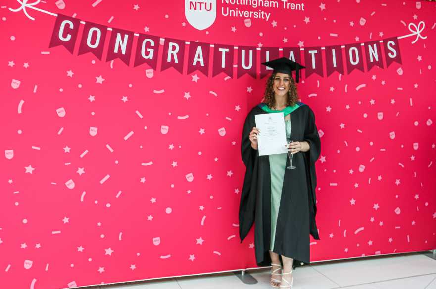Abbie smiling and standing under the NTU graduation sign