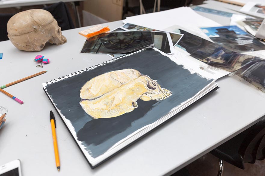 An open sketchbook with a pastel drawing of a skull
