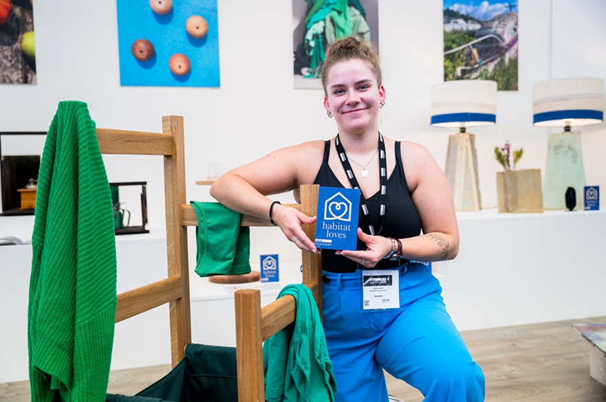 A person sitting next to an item of furniture they designed, and holding an award