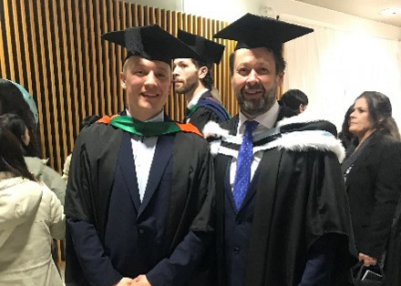 Student George and NTU academic Keith Lown posing for a photograph wearing their graduation gowns.