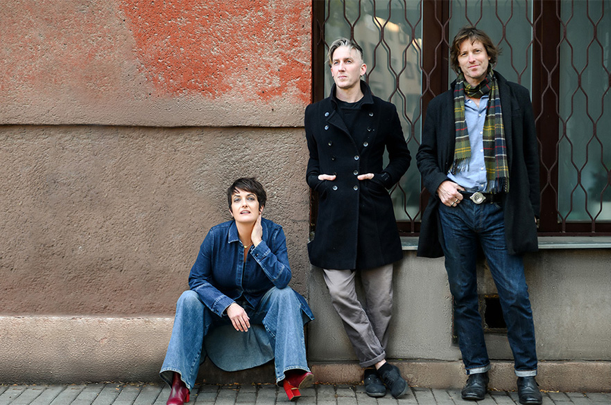 The three band members of Kosheen stood outside leaning against a wall.
