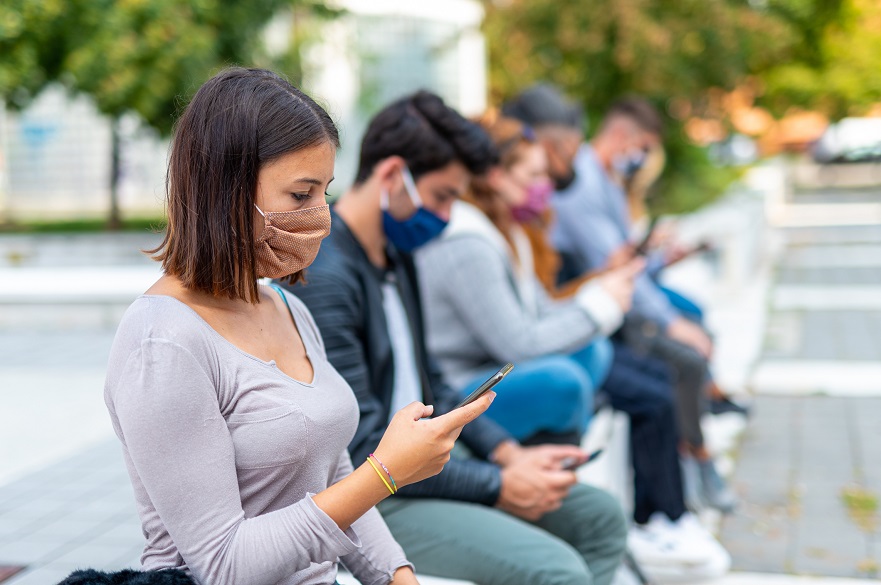 People sitting on a wall in masks looking at mobile phones