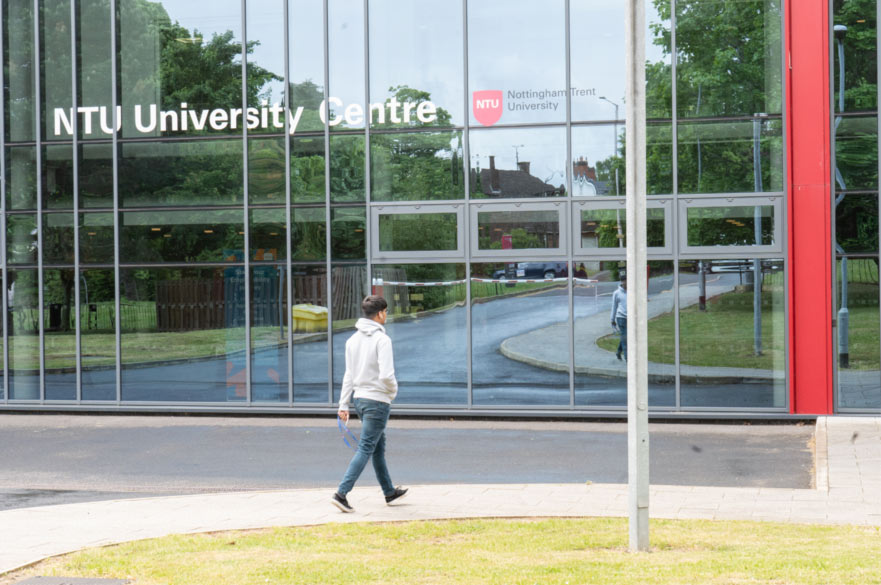The glass front of the NTU Mansfield University Centre, with a student in a grey hoodie walking towards it.