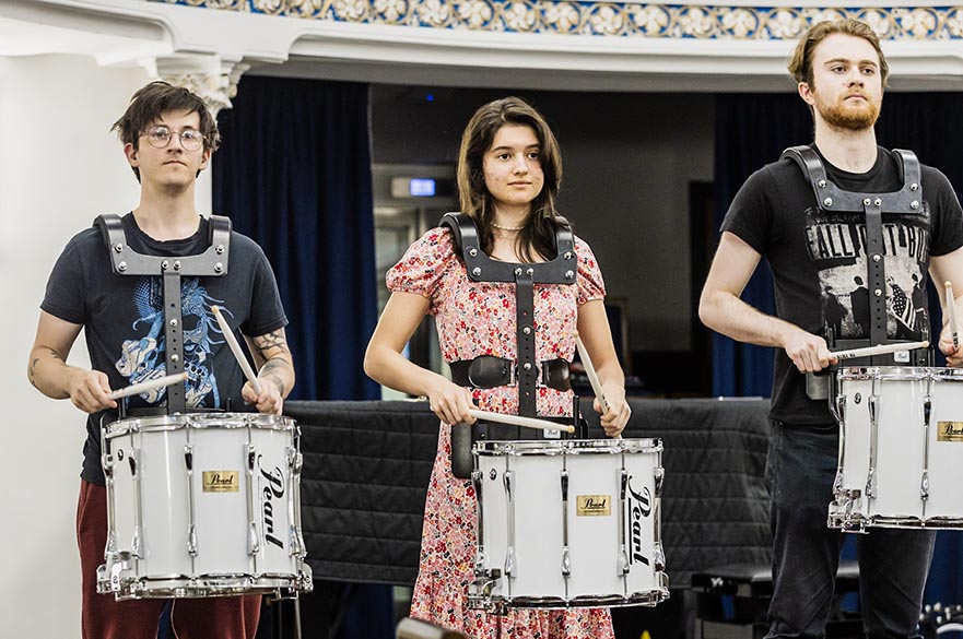 Three students stood on stage with snare drums and drum sticks.