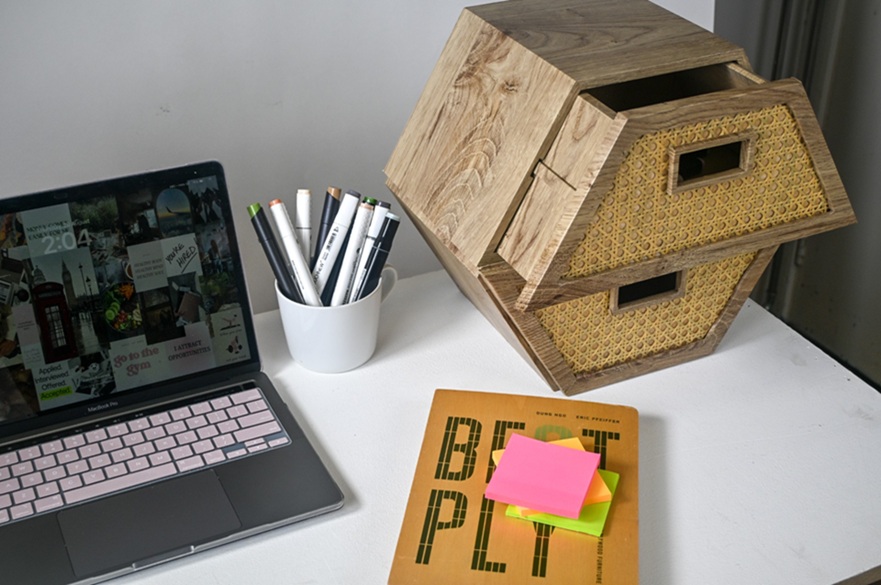 A student's desk with a laptop, stationery, books and two wooden storage boxes stacked one on top of the other.