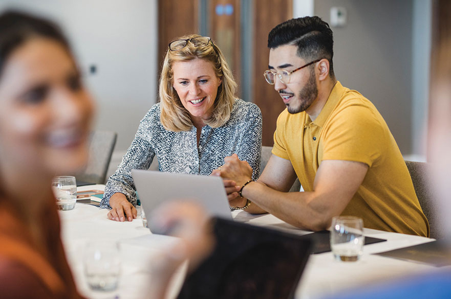 Two people sitting at a table looking at a laptop and having a discussion