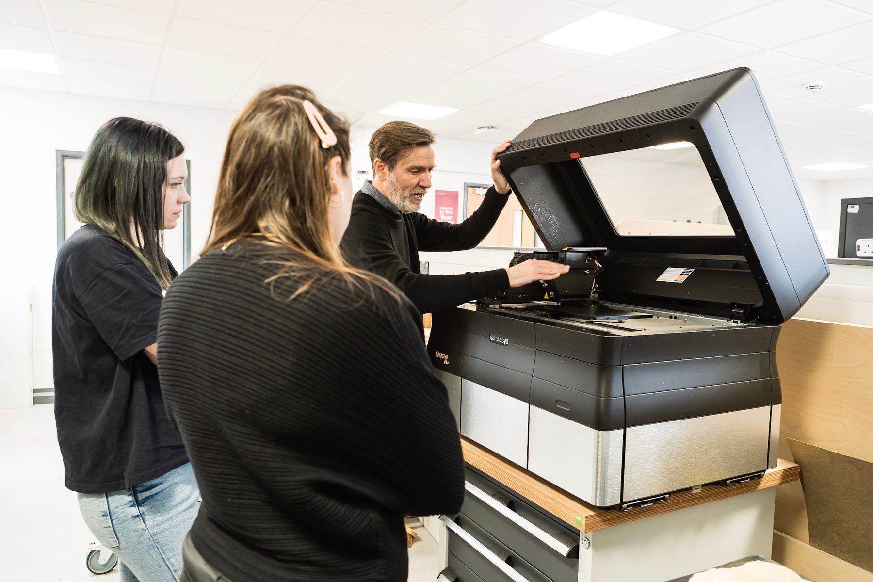 A tutor is showing two students a large digital printing machine