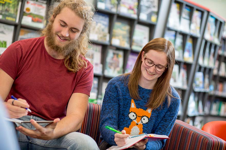 students sat on sofa in library writing in notebooks