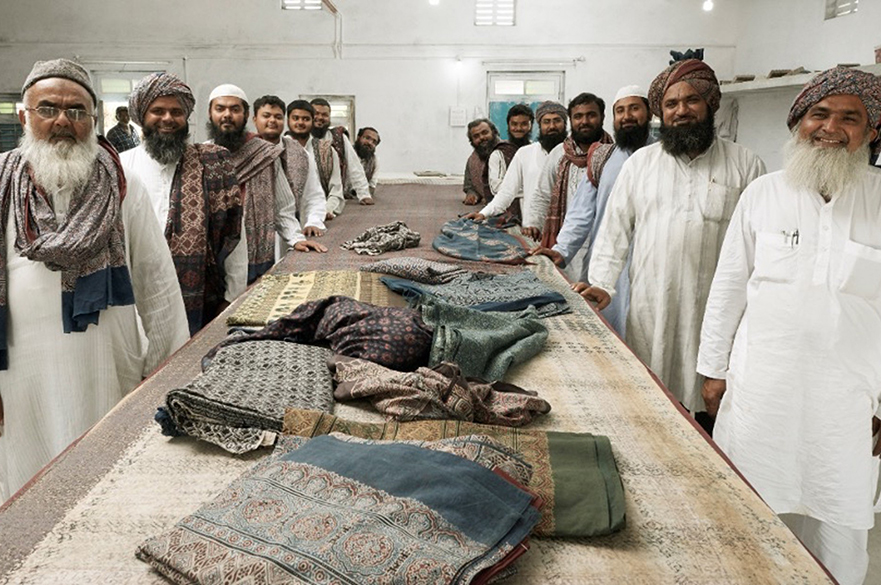 Group of Indian men are standing around a rectangular table smiling and proud of their Indian crafts being presented in the middle. 