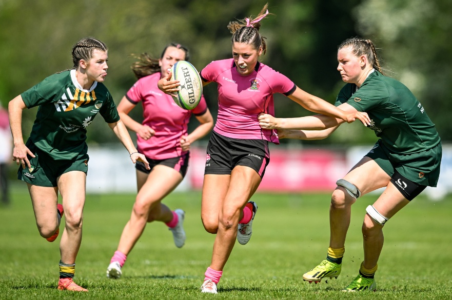 A women's rugby player breaking through a challenge