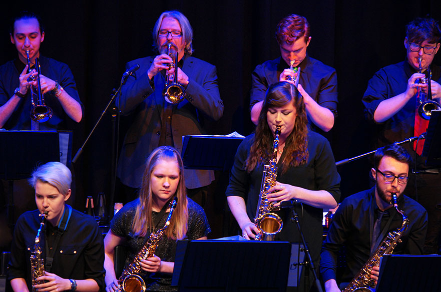 Male and female musicians stood in two lines playing trumpets and saxophones.