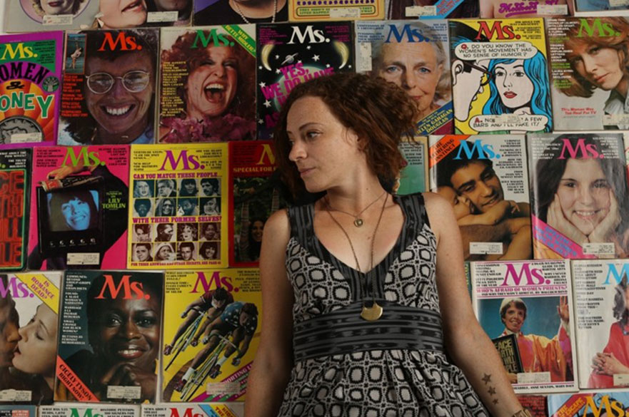 A woman looking to her right, pictured in front of a collection of Ms Magazines