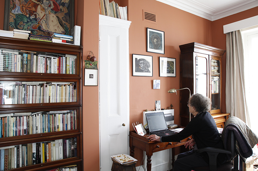 Ruth Fainlight sitting at her desk on a laptop in an office with orange coloured walls