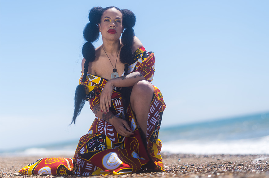 A woman posing crouched down on the beach.