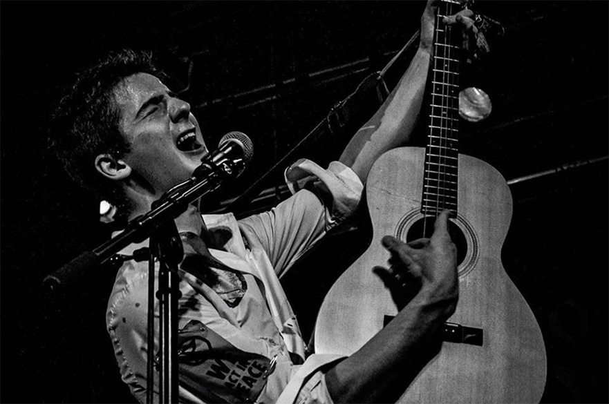 A black and white image of a man singing and playing the acoustic guitar.