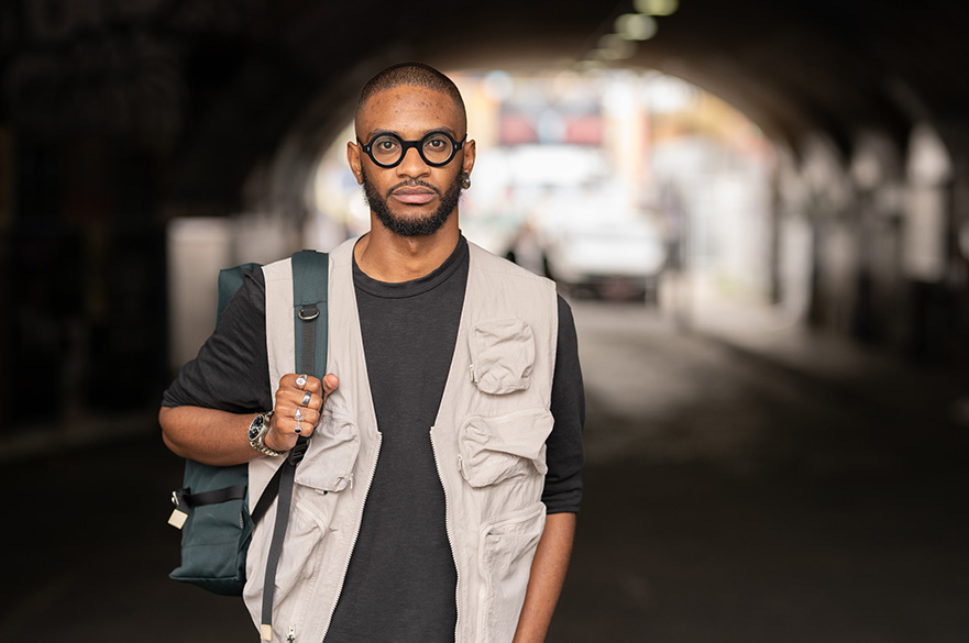 A man stood under a tunnel, holding a backpack over one shoulder.