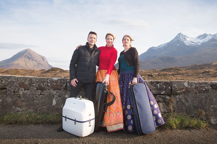 Three musicians stood with their instruments with mountains in the background.