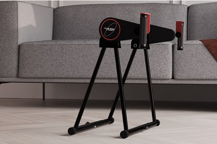 A handcycle trainer on the floor in a room next to a sofa.