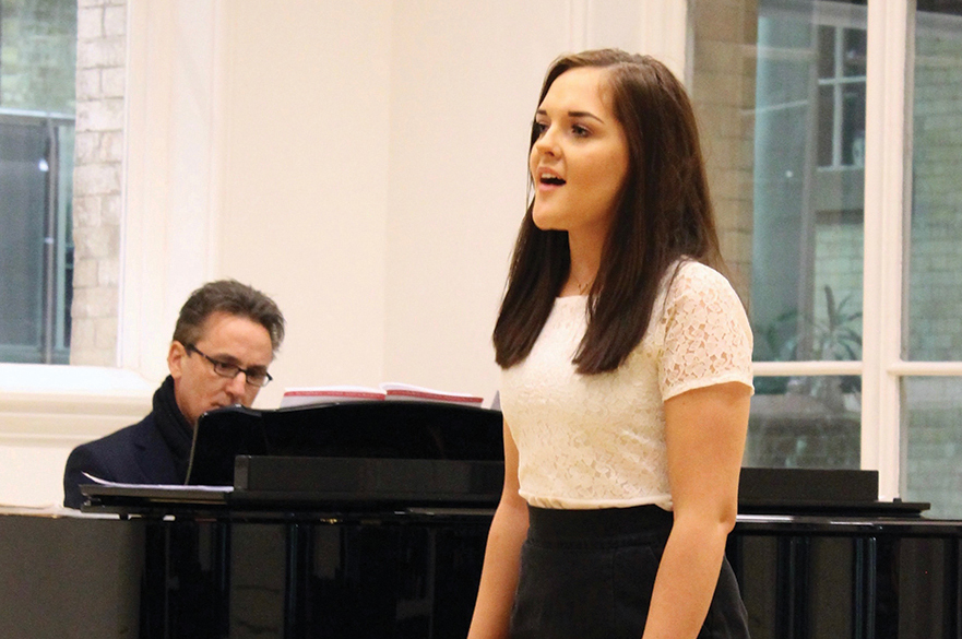 Female student singing in front of a grand piano.
