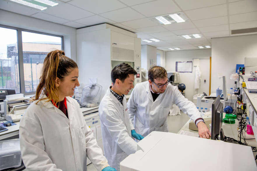 Two research students in lab coats with their supervisor in the lab.