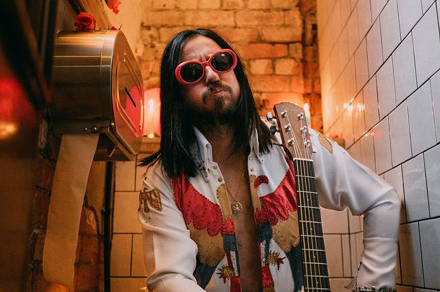 A member of ELVANA (Elvis fronted Nirvana) sitting down with his guitar.