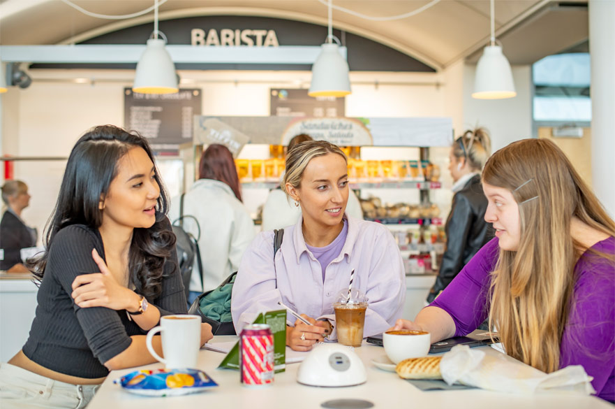 Three students sitting at a table in the Barista Cafe at Clifton Campus