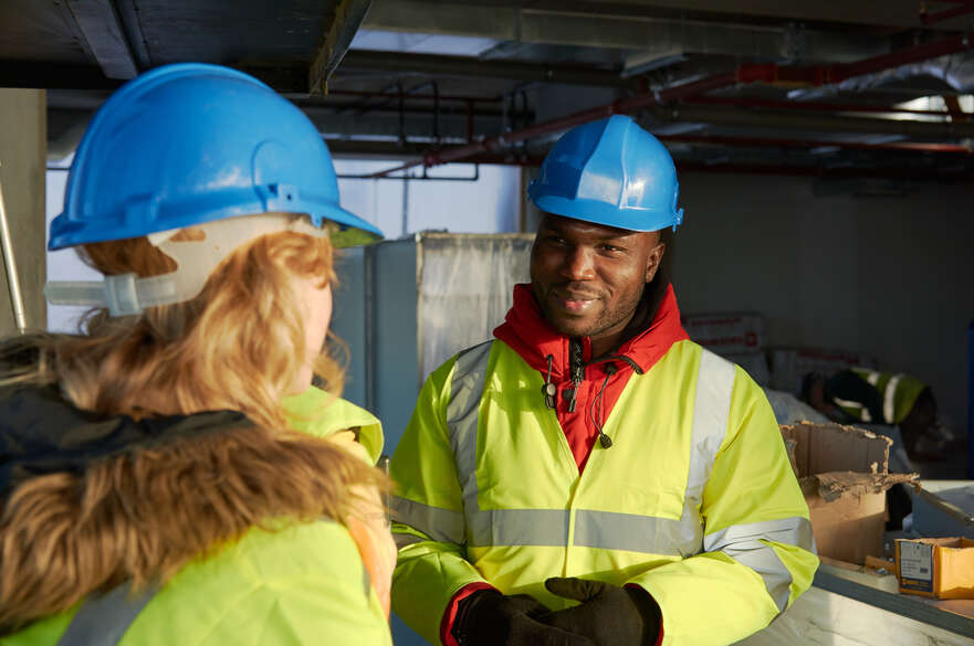Construction student wearing a hard hat and a high viz chatting to a fellow students in a construction site