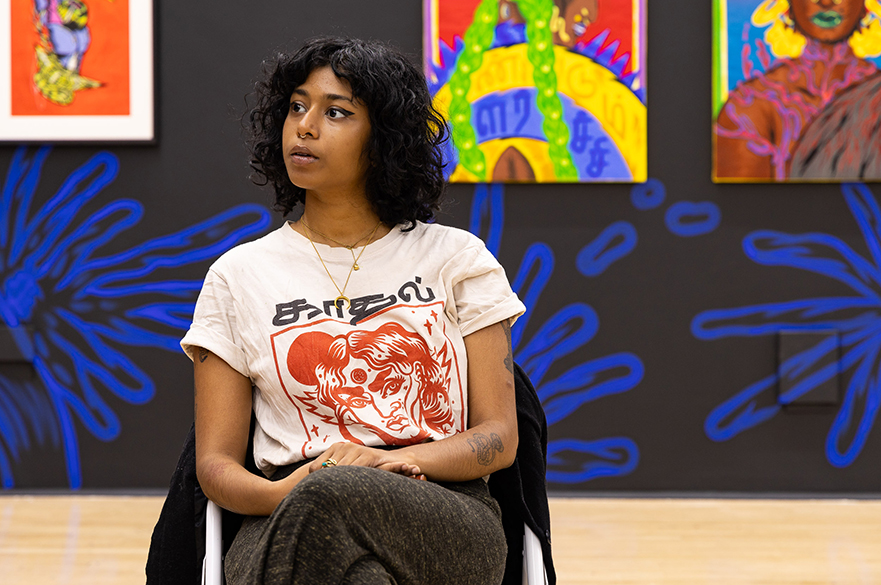 A female with dark curly hair sat on a chair in an art gallery.