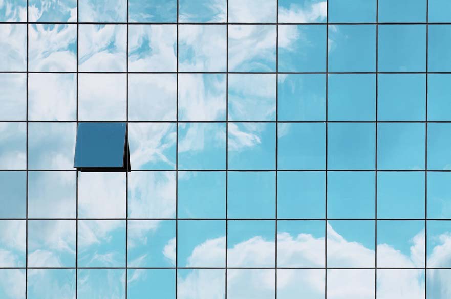 A blue sky and clouds are reflected in a paneled building.