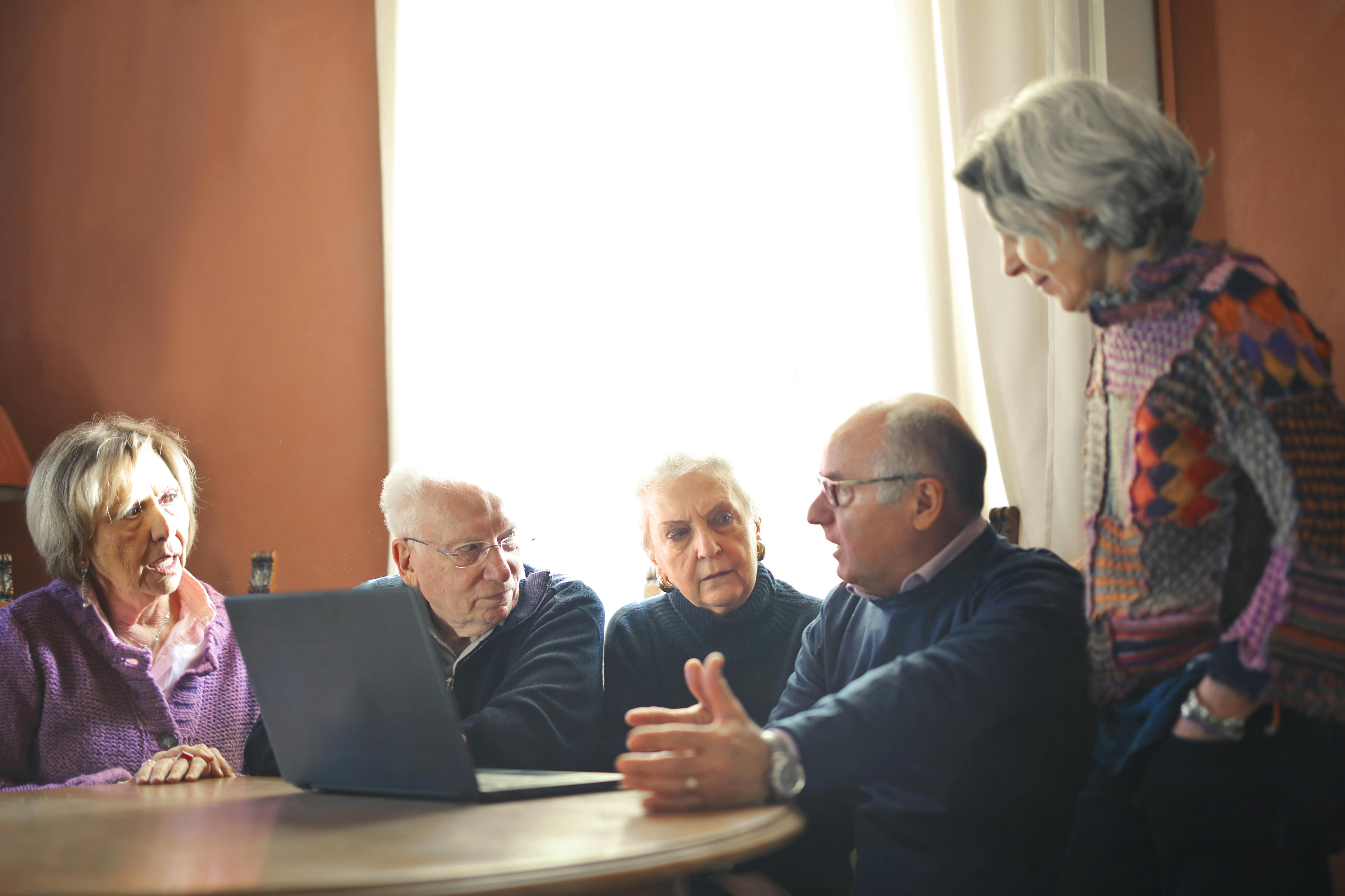 Photo showing 5 older people in conversation around a laptop