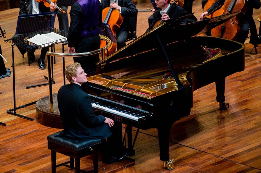 Joseph Moog sat at a piano in front of an orchestra.