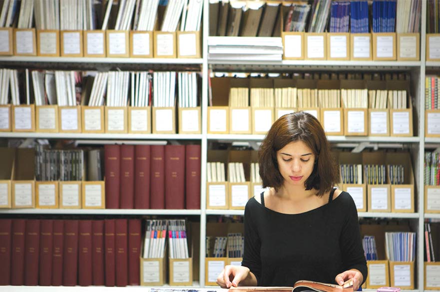 Student reading journal in front of shelves of books and publications