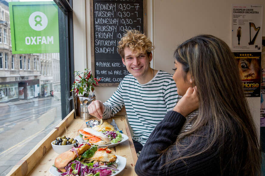 Two students smiling in the window of Ugly Bread Bakery, about to eat their vibrant plates of food.