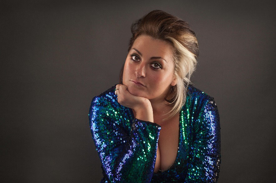 A photo of a woman with her head resting on one hand, wearing a blue sparkly dress.