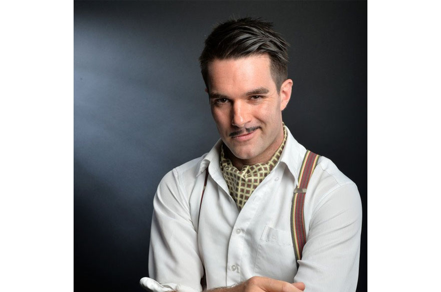 Troy Hawke dressed in a shirt, cravat and braces smiling at the camera.