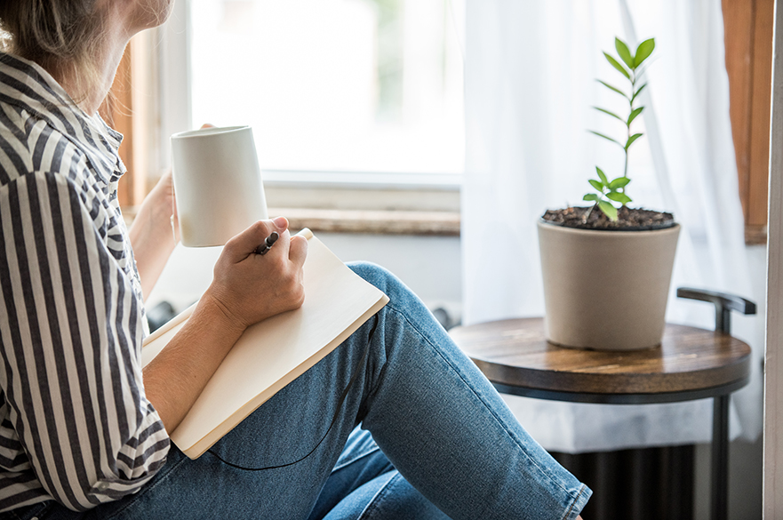 A girl sat with a notebook on her lap, holding a mug.