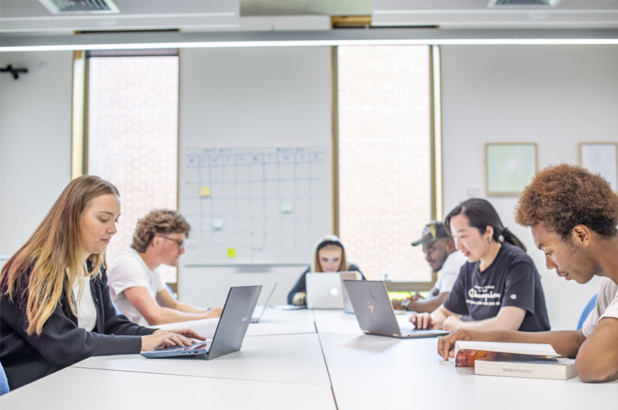 A group of six students working quietly around a table on their laptops.