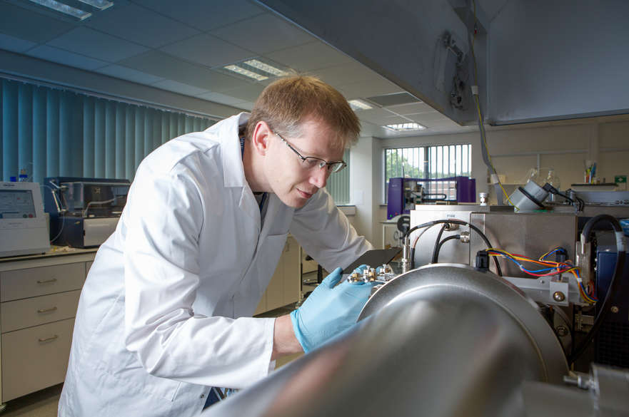 A lab-coated researcher wearing blue plastic gloves as he works on something technical in the lab.