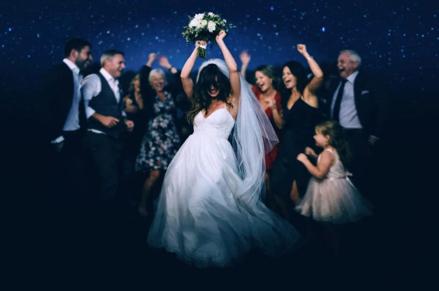 A woman in a wedding dress holding a bouquet of flowers above her head.