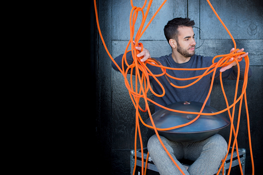 Manu Delago sat with his hang on his lap, and some orange rope in front of him.