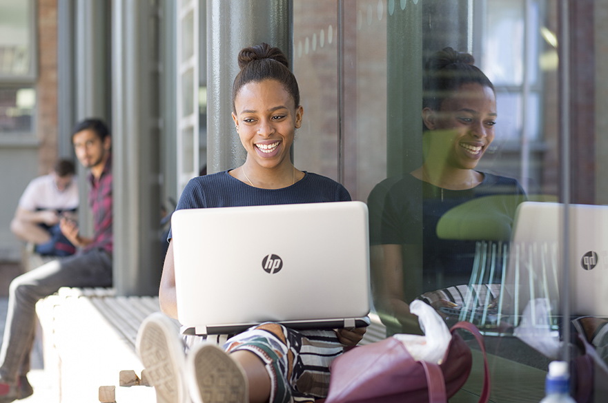 Smiling girl sat with a laptop on her knees.