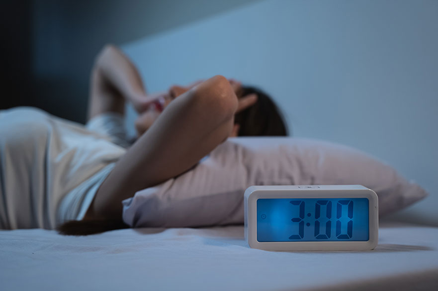 Woman awake in bed with clock showing 3am