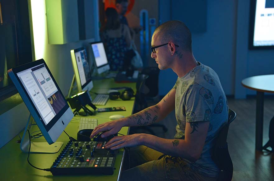 Male student sat at desk working on a MAC computer