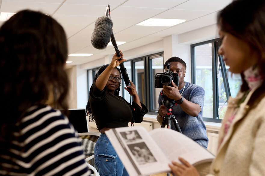 Two students filming students reading a book