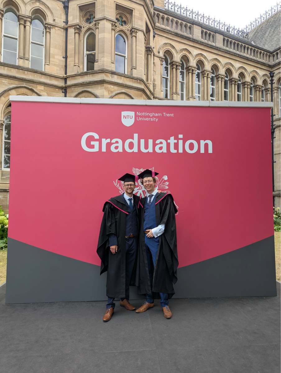George and Sam posing at Graduation in front of a large Graduation sign.