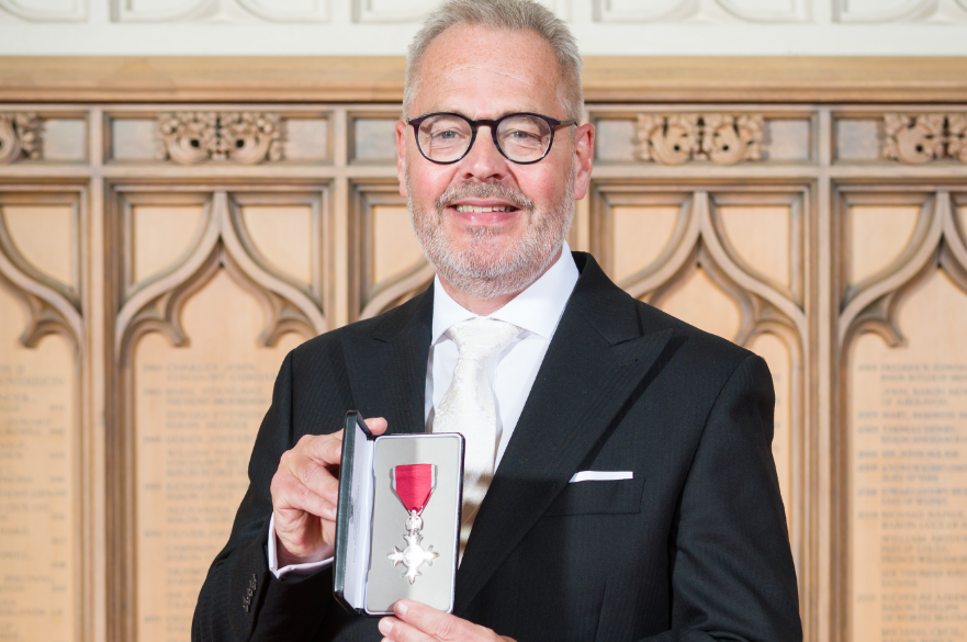 Kevin Osbon posed for a photo, facing the camera, displaying his MBE.