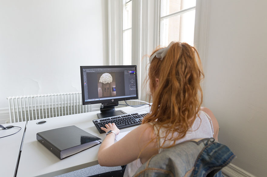 A person sits at a computer, working on a design project.